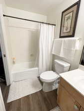 Full bathroom with vanity, a textured ceiling, LVP flooring, shower / bathtub combination with curtain, and toilet