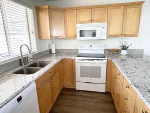 Kitchen with dark LVP floors, Granite countertops, white appliances, and sink