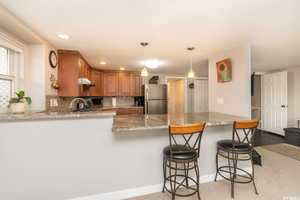 Kitchen featuring kitchen peninsula, backsplash, stainless steel refrigerator, and hanging light fixtures