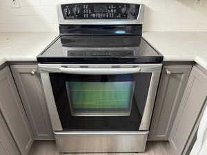 Room details with decorative backsplash, light hardwood / wood-style floors, stainless steel range with electric stovetop, and gray cabinetry