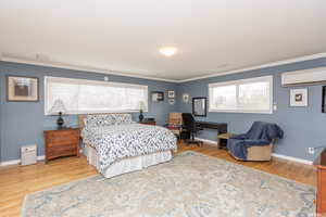 Bedroom with an AC wall unit, multiple windows, wood-type flooring, and ornamental molding