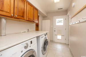 Clothes washing area with washer and dryer, light tile patterned floors, and cabinets