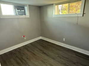 Basement featuring a healthy amount of sunlight, dark wood-type flooring, and cooling unit