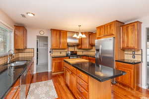 Kitchen with a center island, hanging light fixtures, decorative backsplash, light wood-type flooring, and appliances with stainless steel finishes