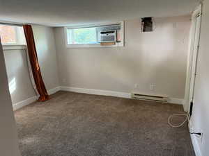 Basement featuring carpet flooring, plenty of natural light, a baseboard radiator, and a textured ceiling