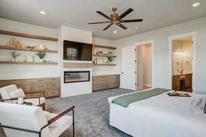 Carpeted bedroom featuring a large fireplace, ensuite bath, and ceiling fan