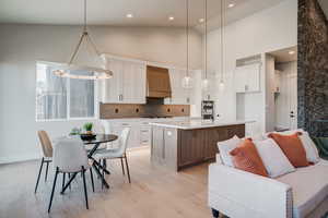 Kitchen with custom range hood, pendant lighting, a center island with sink, high vaulted ceiling, and white cabinets