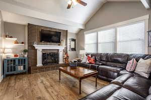 Living room featuring ceiling fan, light hardwood / wood-style floors, lofted ceiling, and a brick fireplace