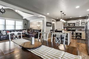 Dining area with a notable chandelier, light wood-type flooring, a textured ceiling, and vaulted ceiling