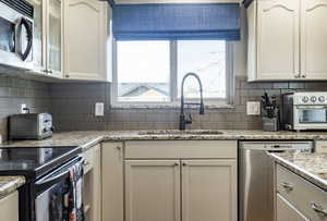 Kitchen with decorative backsplash, appliances with stainless steel finishes, white cabinetry, and light stone countertops