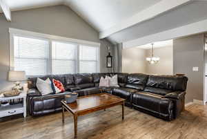 Living room featuring wood-type flooring, an inviting chandelier, vaulted ceiling, and a wealth of natural light