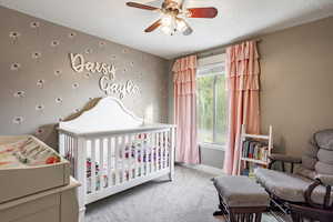 Bedroom featuring a crib, carpet, a textured ceiling, and ceiling fan