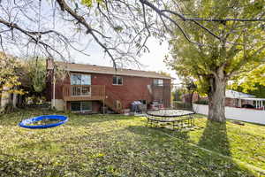 Rear view of house with a lawn, central air condition unit, a wooden deck, and a trampoline