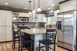 Kitchen featuring appliances with stainless steel finishes, light wood-type flooring, white cabinets, a center island, and hanging light fixtures