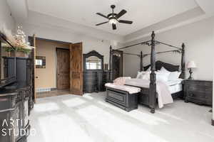 Carpeted bedroom with a tray ceiling and ceiling fan