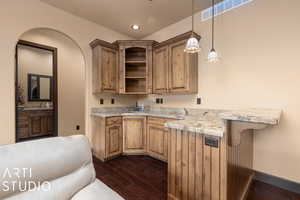 Kitchen with a kitchen breakfast bar, light stone counters, dark hardwood / wood-style floors, kitchen peninsula, and decorative light fixtures