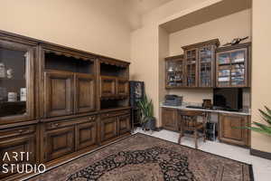 Home office featuring light carpet, a towering ceiling, and built in desk