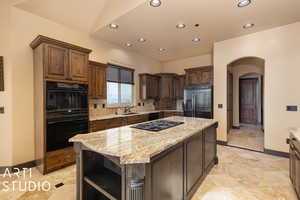 Kitchen featuring light stone counters, stainless steel fridge, black double oven, decorative backsplash, and a kitchen island