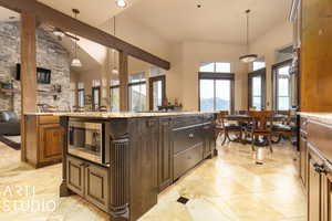 Kitchen with hanging light fixtures, high vaulted ceiling, a mountain view, stainless steel microwave, and an island with sink