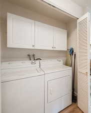 Laundry room with cabinets, light wood-type flooring, and washer and clothes dryer