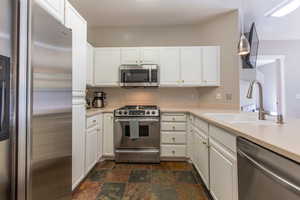 Kitchen with sink, hanging light fixtures, stainless steel appliances, kitchen peninsula, and white cabinets