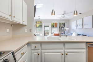 Kitchen with kitchen peninsula, sink, stainless steel range oven, white cabinetry, and hanging light fixtures