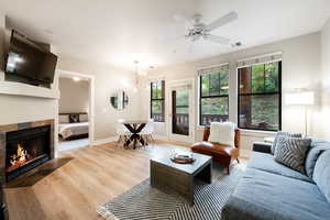 Living room with light wood-type flooring, ceiling fan, and a tiled fireplace