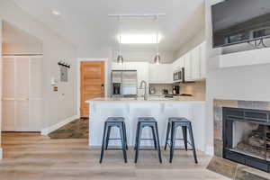 Kitchen featuring a breakfast bar, white cabinets, light hardwood / wood-style flooring, appliances with stainless steel finishes, and kitchen peninsula