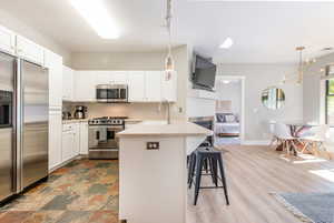 Kitchen featuring kitchen peninsula, white cabinetry, pendant lighting, and stainless steel appliances