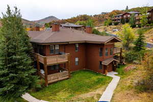 Rear view of house featuring a mountain view, a balcony, and a lawn