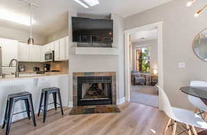 Kitchen featuring white cabinets, sink, light hardwood / wood-style flooring, a breakfast bar area, and a tiled fireplace