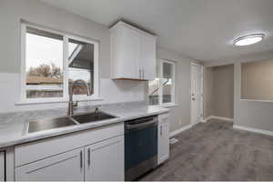 Kitchen with sink, white cabinets, stainless steel dishwasher, and light hardwood / wood-style floors