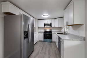 Kitchen with white cabinets, sink, stainless steel appliances, and light hardwood / wood-style flooring