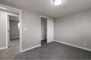 Unfurnished bedroom featuring dark colored carpet, a textured ceiling, and a closet