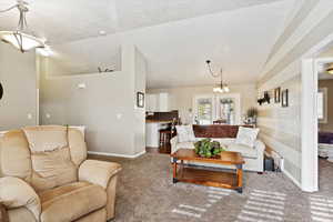 Carpeted living room with a textured ceiling, lofted ceiling, and a notable chandelier