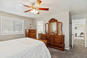 Carpeted bedroom with connected bathroom, ceiling fan, and a textured ceiling