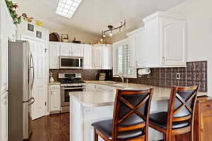 Kitchen with white cabinetry, sink, stainless steel appliances, kitchen peninsula, and a breakfast bar area