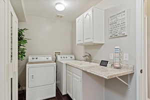 Clothes washing area featuring cabinets, a textured ceiling, dark wood-type flooring, sink, and washing machine and dryer