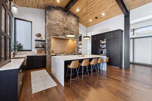 Kitchen with decorative light fixtures, high vaulted ceiling, wooden ceiling, dark hardwood floors, and a kitchen island