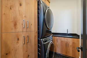 Laundry room with cabinets, stacked washing maching and dryer, and sink