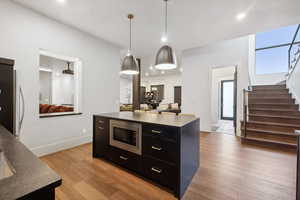 Kitchen featuring light wood-type flooring, stainless steel appliances, a kitchen island, and hanging light fixtures