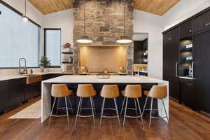 Kitchen featuring Farmhouse sink, dark hardwood flooring, wooden ceiling, pendant lighting, and a center island with seating