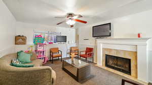 Living room featuring carpet flooring, ceiling fan, and a tiled fireplace