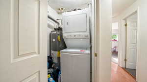 Laundry room featuring a textured ceiling, water heater, light hardwood / wood-style floors, and stacked washer and clothes dryer