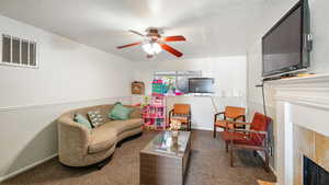 Carpeted living room featuring ceiling fan and a tiled fireplace