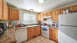 Kitchen featuring sink, a textured ceiling, white appliances, and light tile patterned flooring