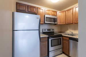 Kitchen featuring light stone countertops, sink, light tile patterned floors, and appliances with stainless steel finishes