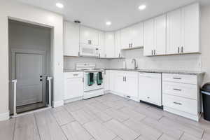 Kitchen featuring white cabinets, white appliances, and light stone countertops