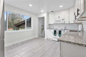 Kitchen with sink, light stone counters, light hardwood / wood-style floors, white appliances, and white cabinets