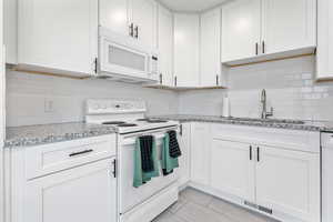 Kitchen featuring white appliances, sink, decorative backsplash, light stone counters, and white cabinetry